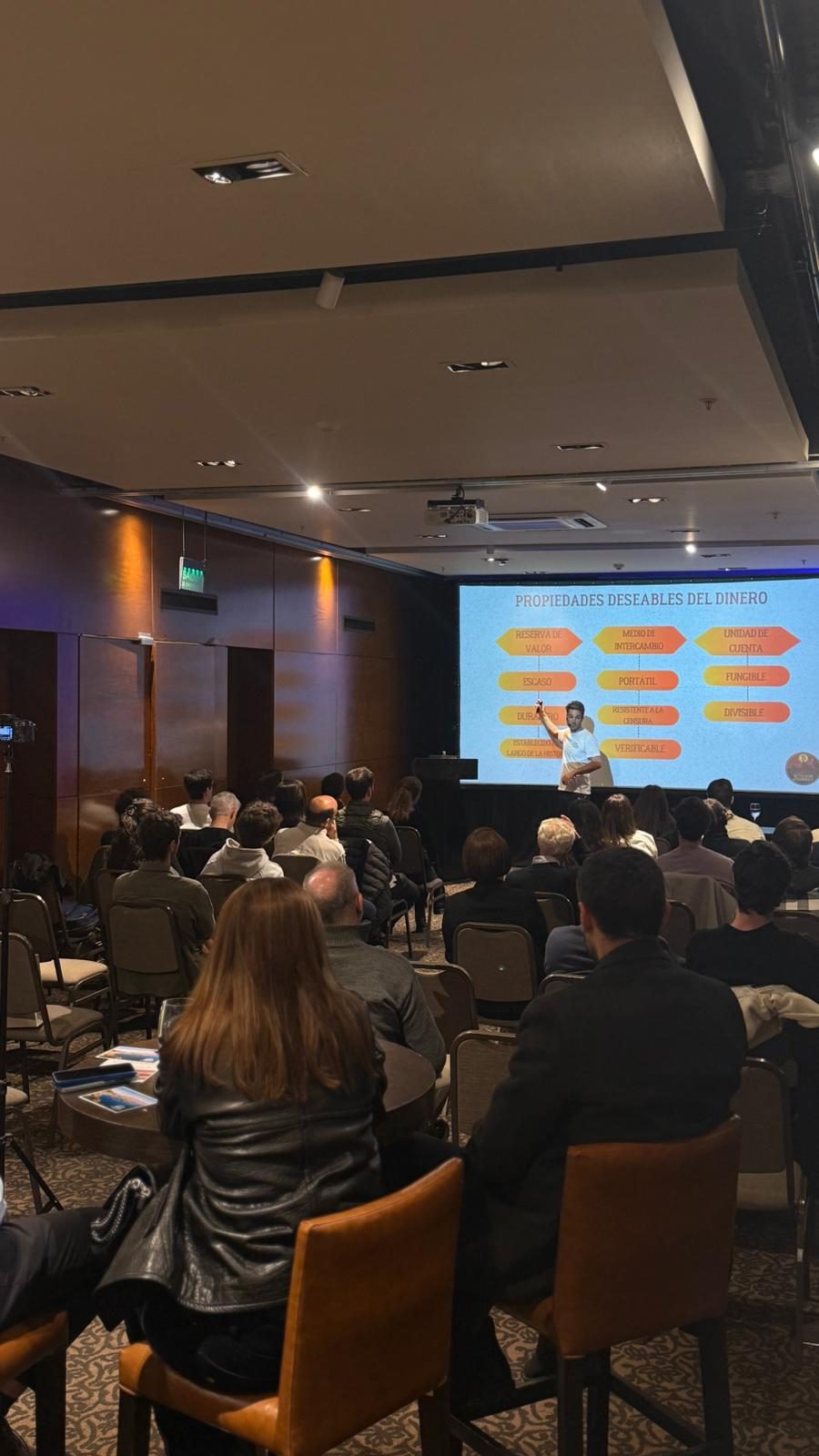 A Bitcoin Journey session in a hotel function room, with a slide on the properties of money shown in Spanish.