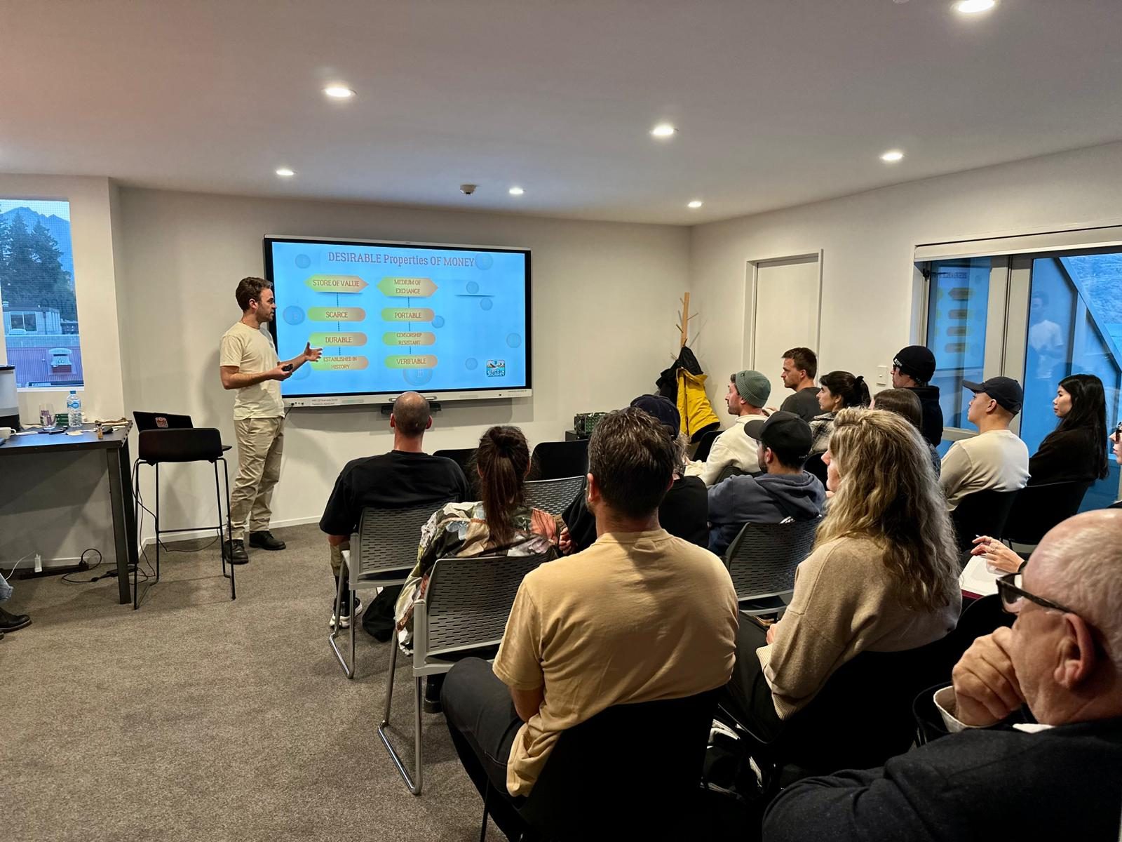 A presenter talking through a slide headed "Desirable properties of money" to a room of seated attendees.