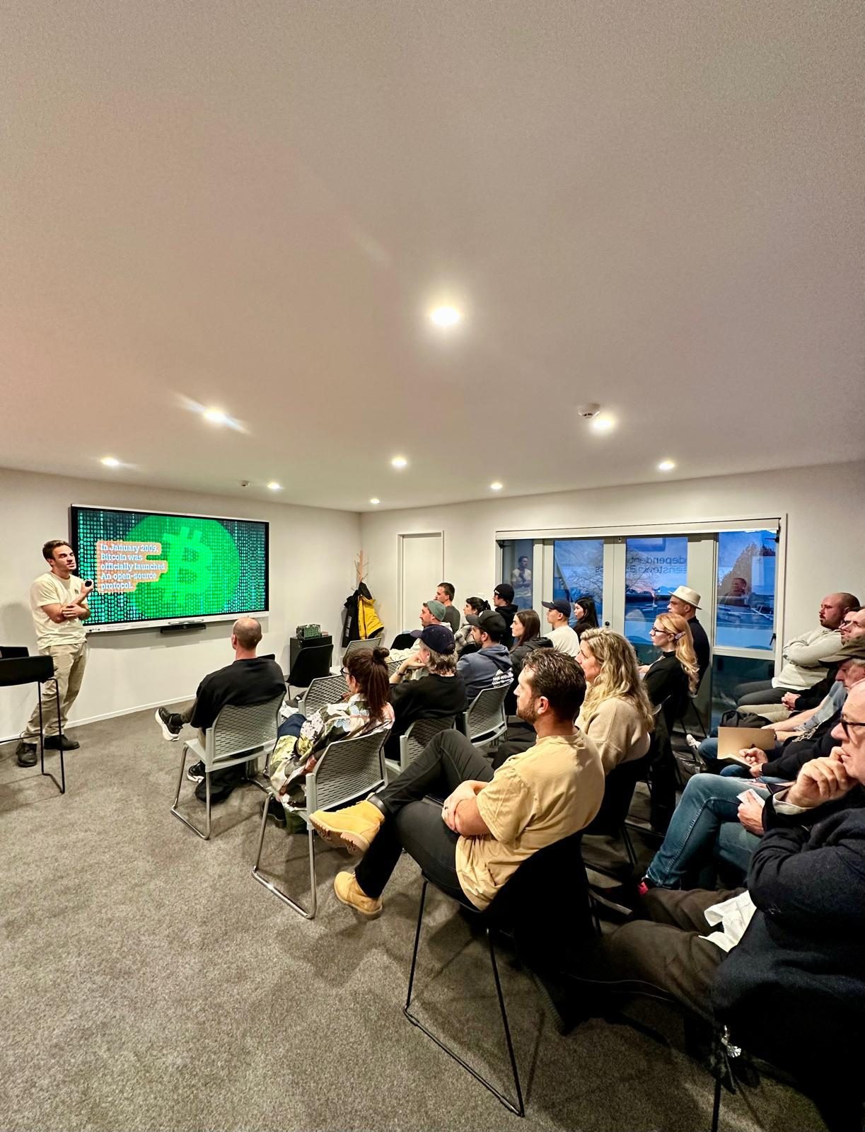 A full room of attendees watching a slide about Bitcoin's launch as an open-source protocol in January 2009.